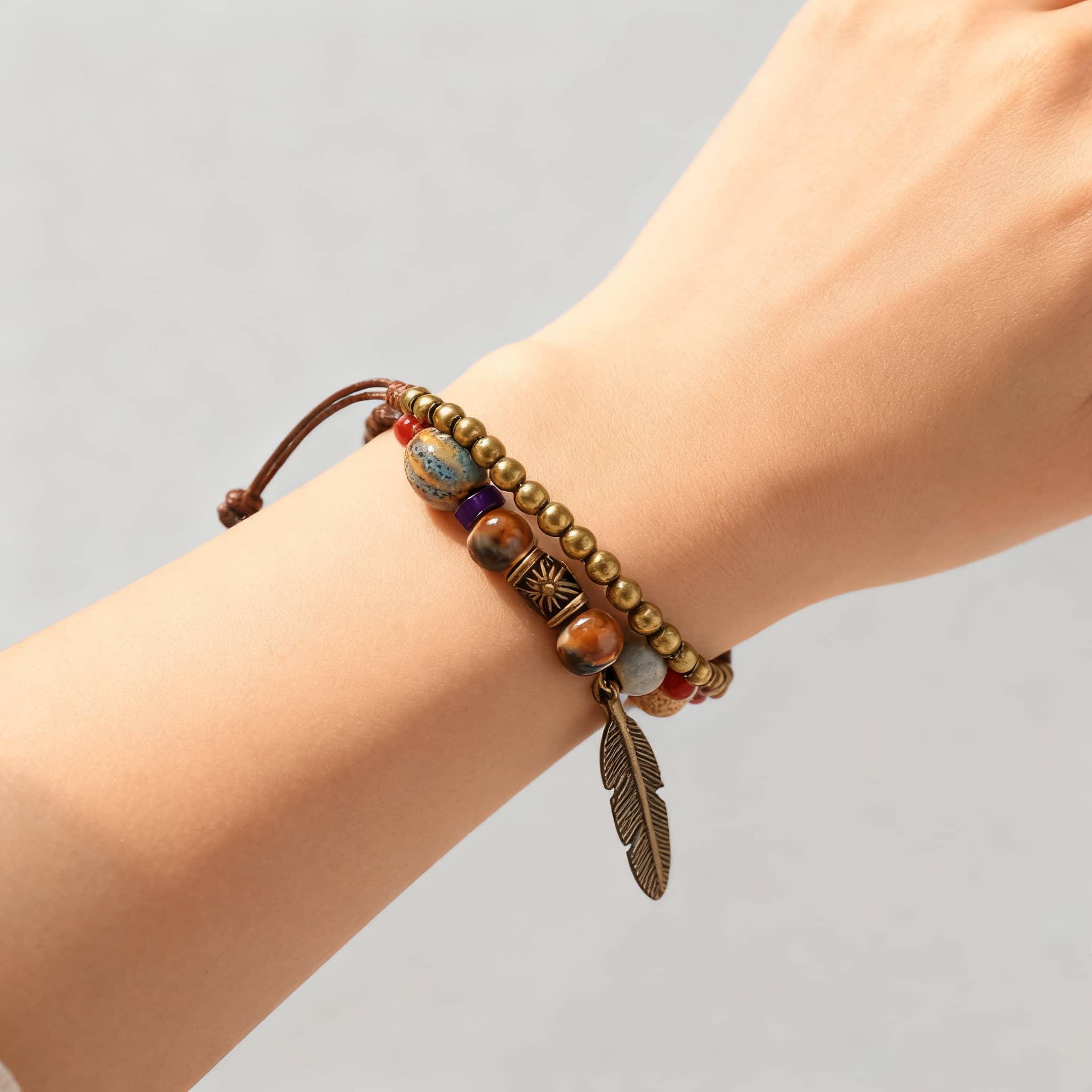 Handmade bell and bead bracelet featuring colorful beads and a feather charm on a brown cord