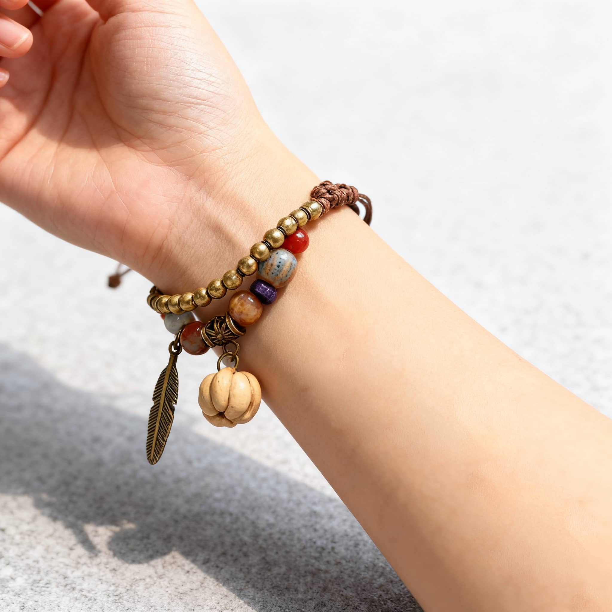 Hand wearing a hawthorn seed ceramic bracelet with colorful beads and a feather charm