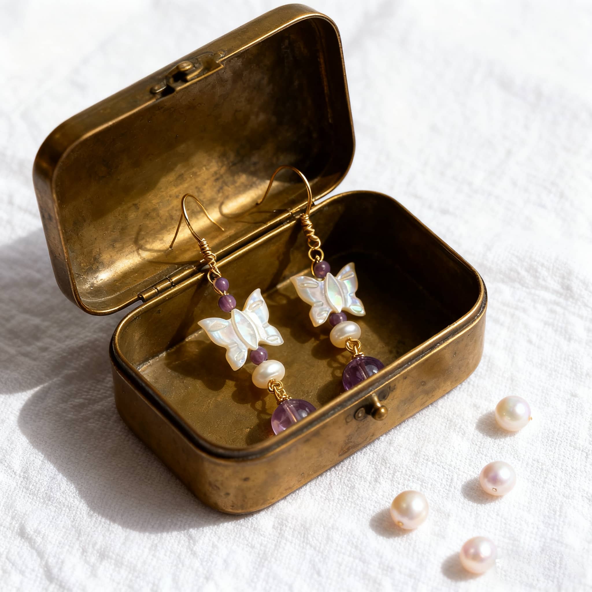 Amethyst butterfly pearl earrings in a vintage box with additional pearls on a soft fabric background