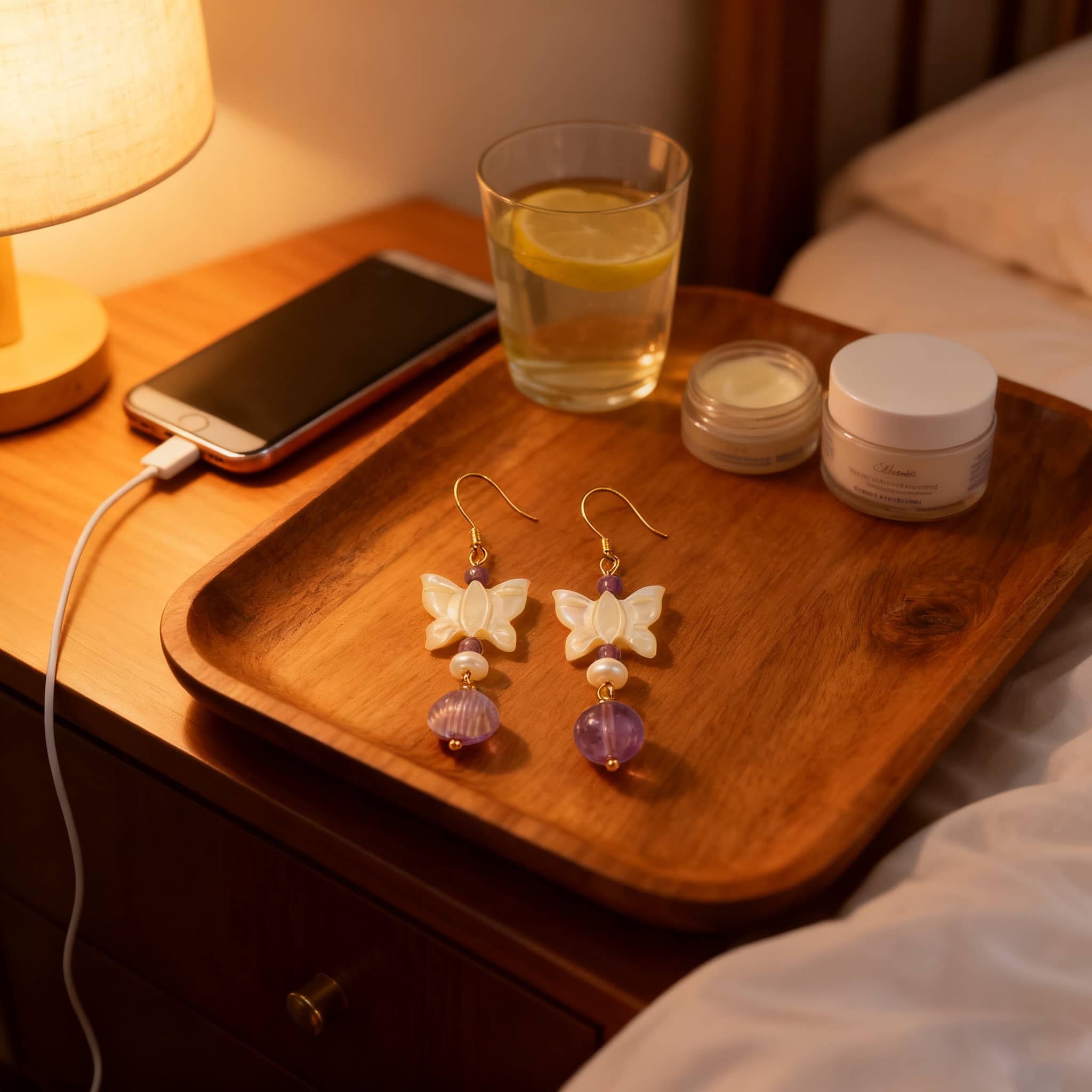 Amethyst butterfly pearl earrings displayed on a bedside table next to a lamp and a glass of water