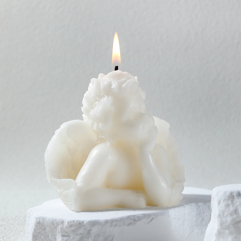 White angel sculpture candle with detailed wings and a lit flame on top