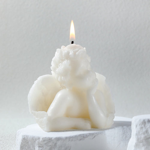 White angel sculpture candle with detailed wings and a lit flame on top
