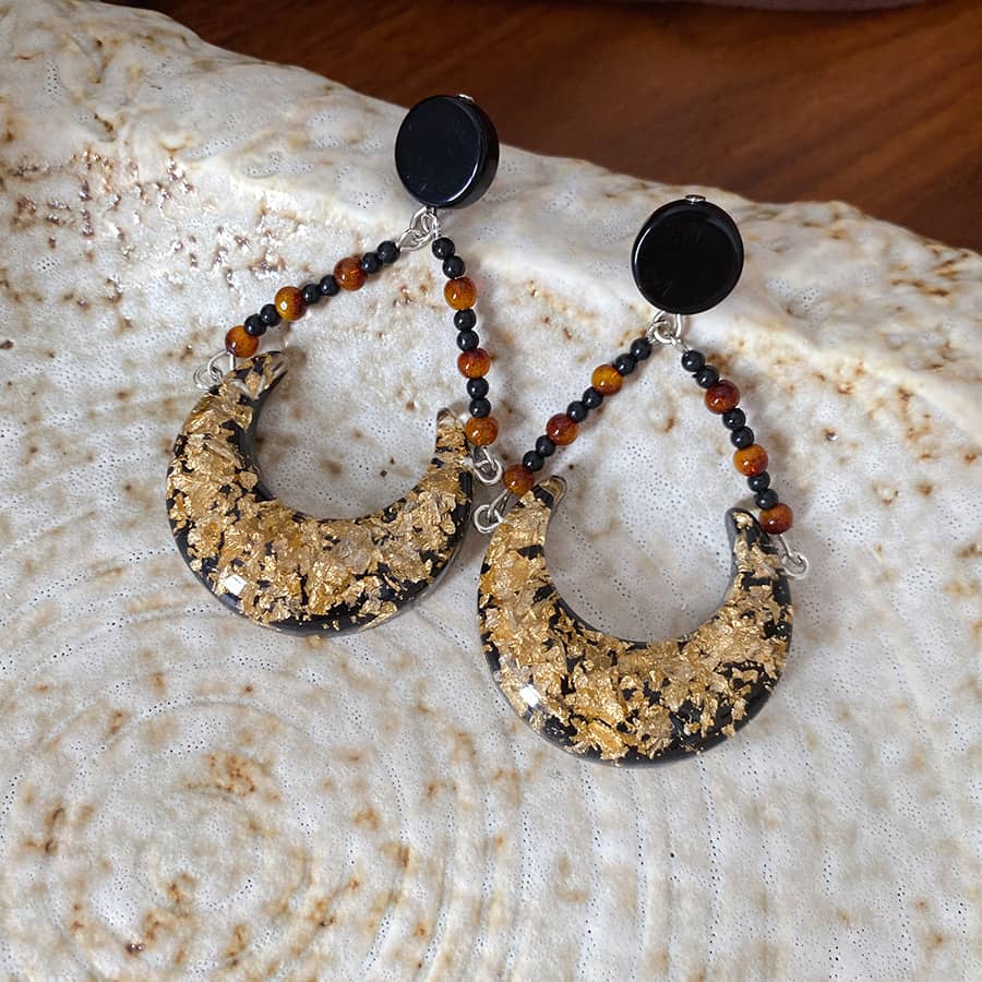 Angry resin moon earrings featuring gold flakes and a unique black bead design