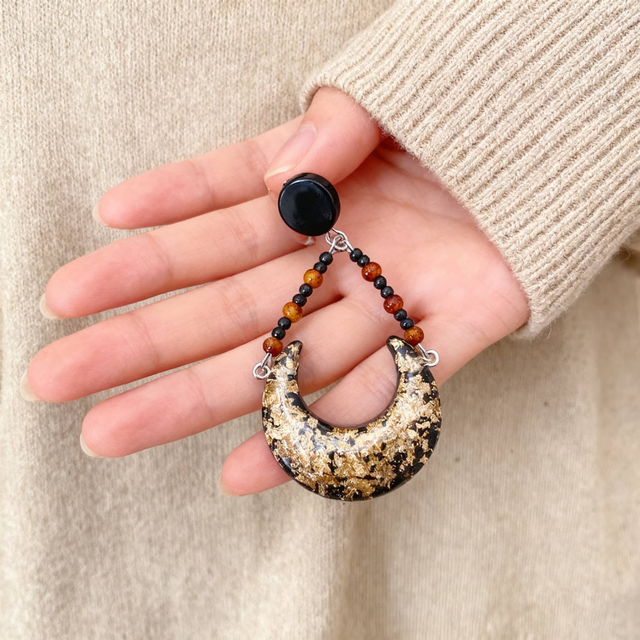 Angry resin moon earrings with gold and black accents, set on a beaded design