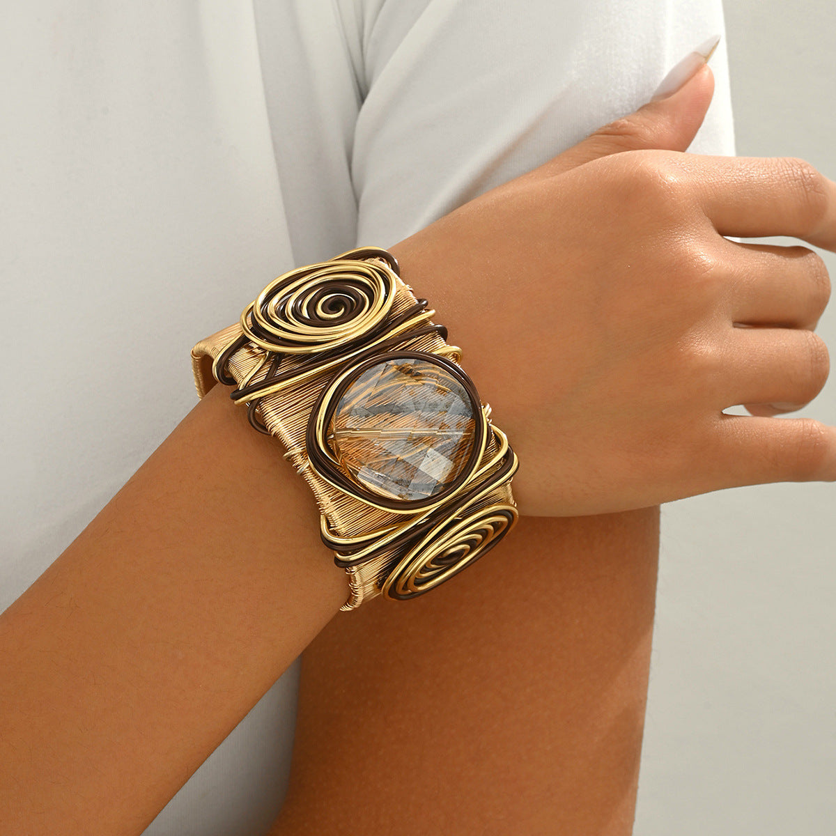 Hand wearing bold gemstone cuff bracelet with gold wire swirl design and round rutilated quartz center