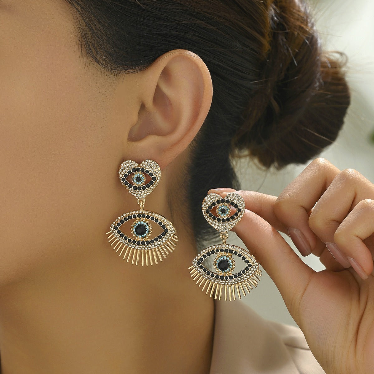 Gold heart angel eye stud earrings with black white crystals and sunray fringe shown on model ear