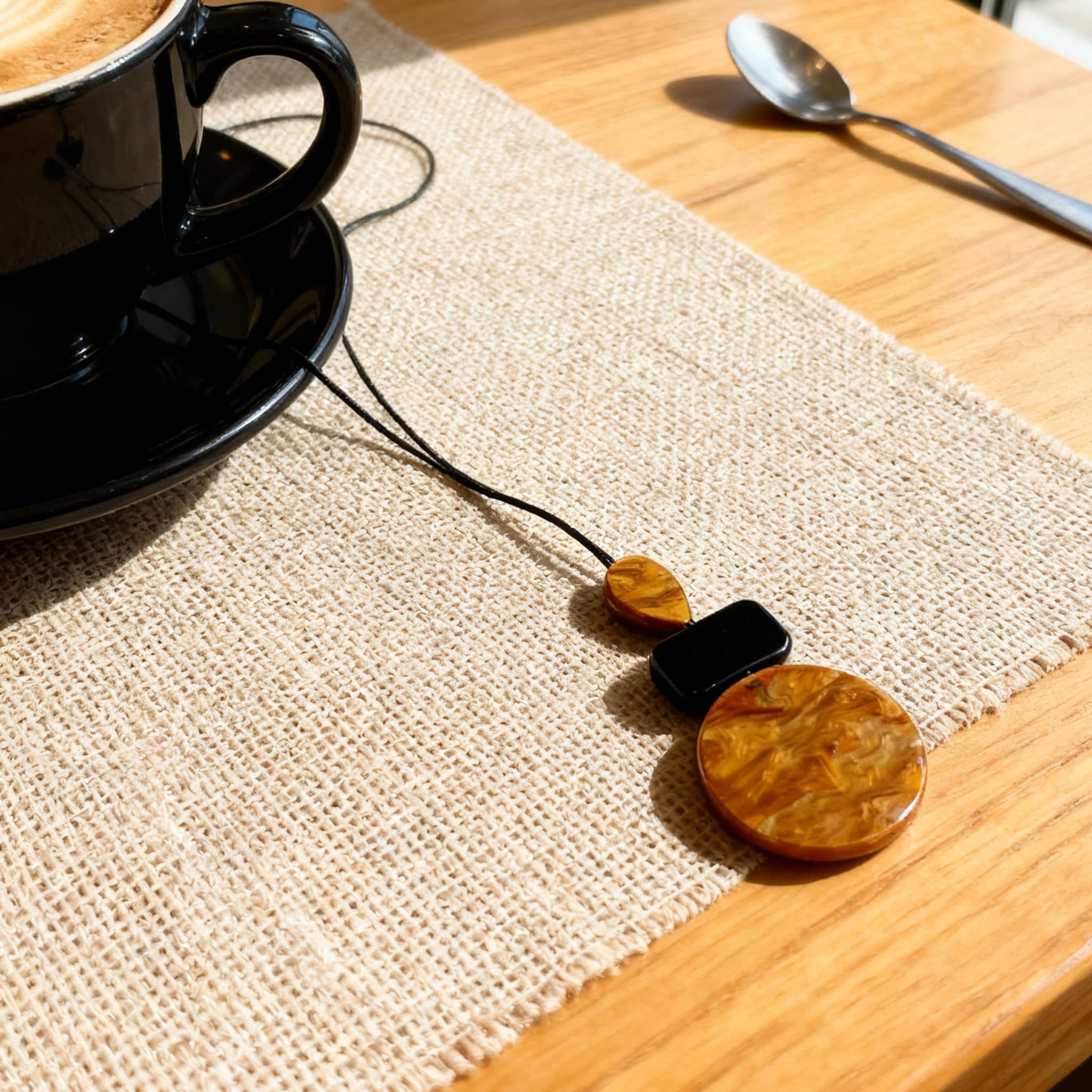 Stylish black and ochre statement jewelry necklace displayed beside a coffee cup on a wooden table