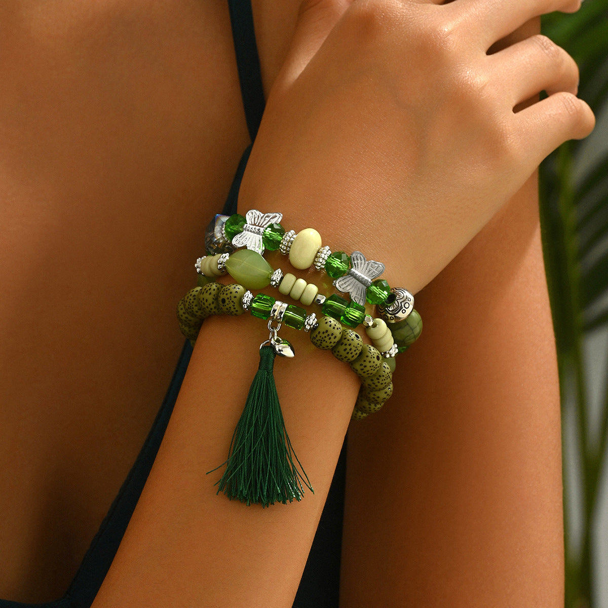 Green beaded bracelet trio stacked on wrist with tassel charm silver butterfly accents and mixed stone beads