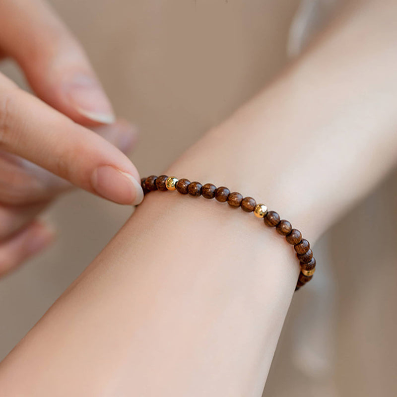 Hand wearing calming silkwood gold bead bracelet with natural wooden beads and gold accents