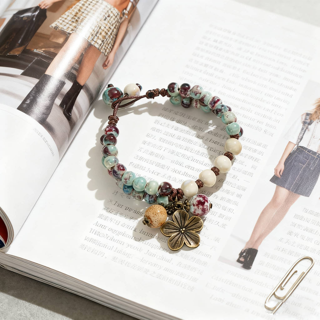 Ceramic floral charm bracelet with assorted beads and a flower charm on an open magazine