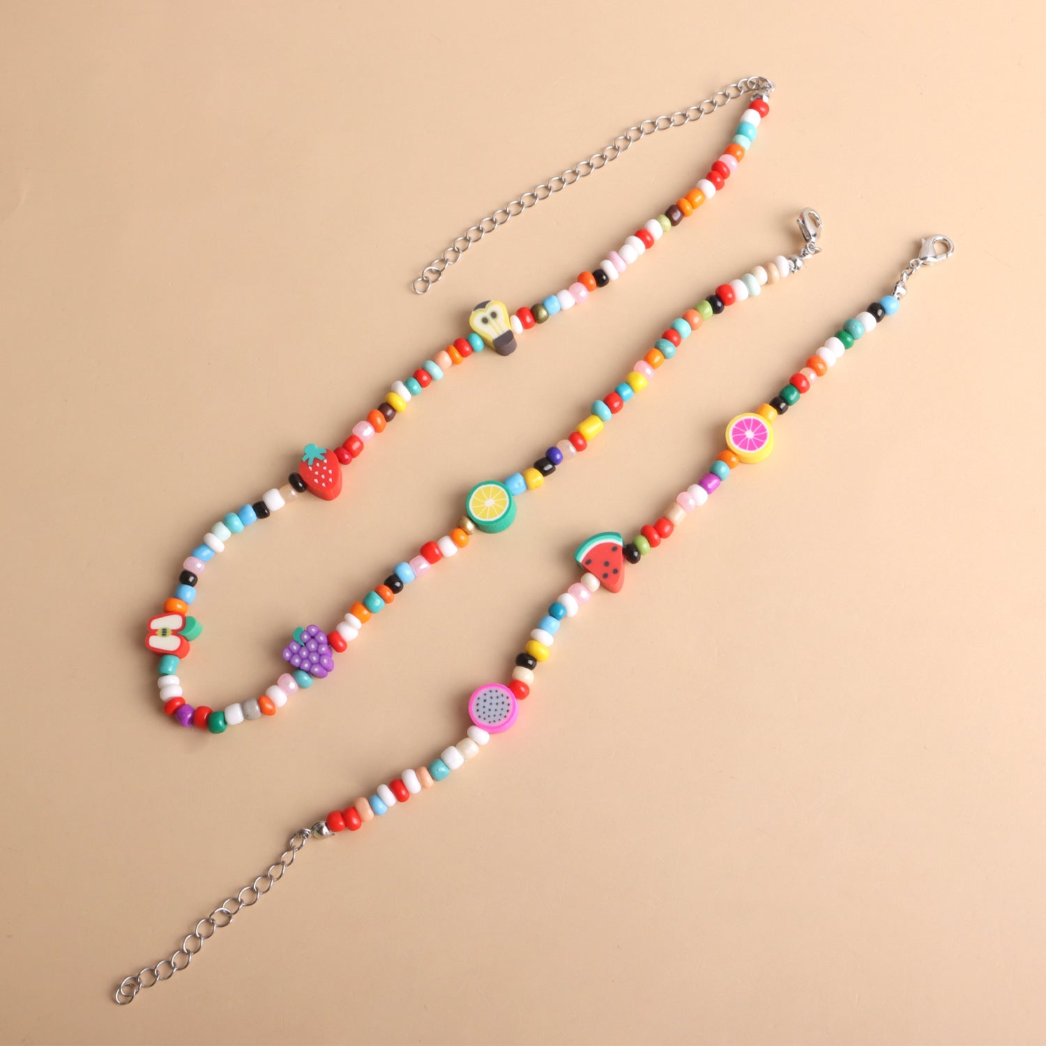 Colorful beaded necklace and bracelet with fruit and heart charms on a beige background