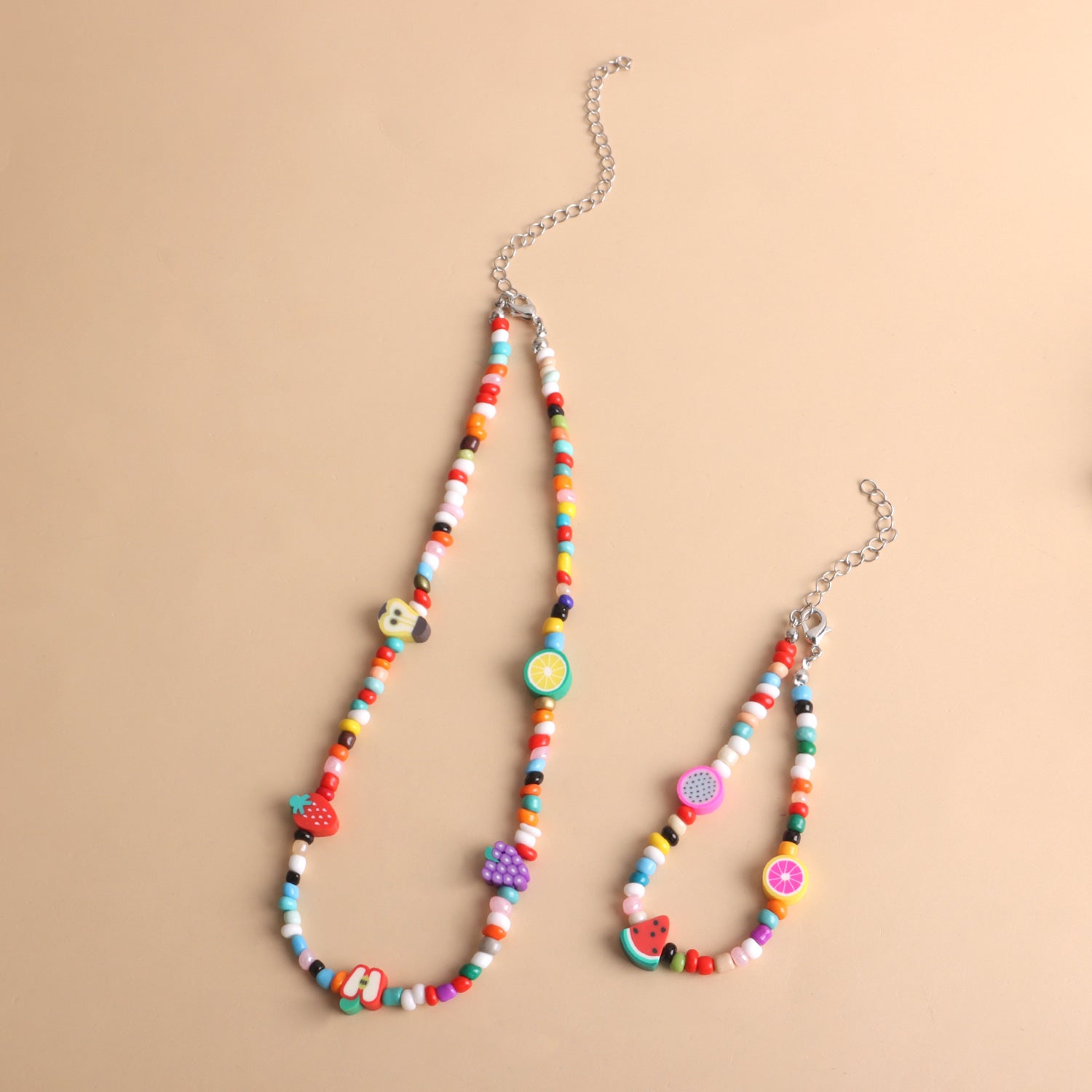 Colorful beaded necklace and bracelet with fruit and animal charm beads on beige background
