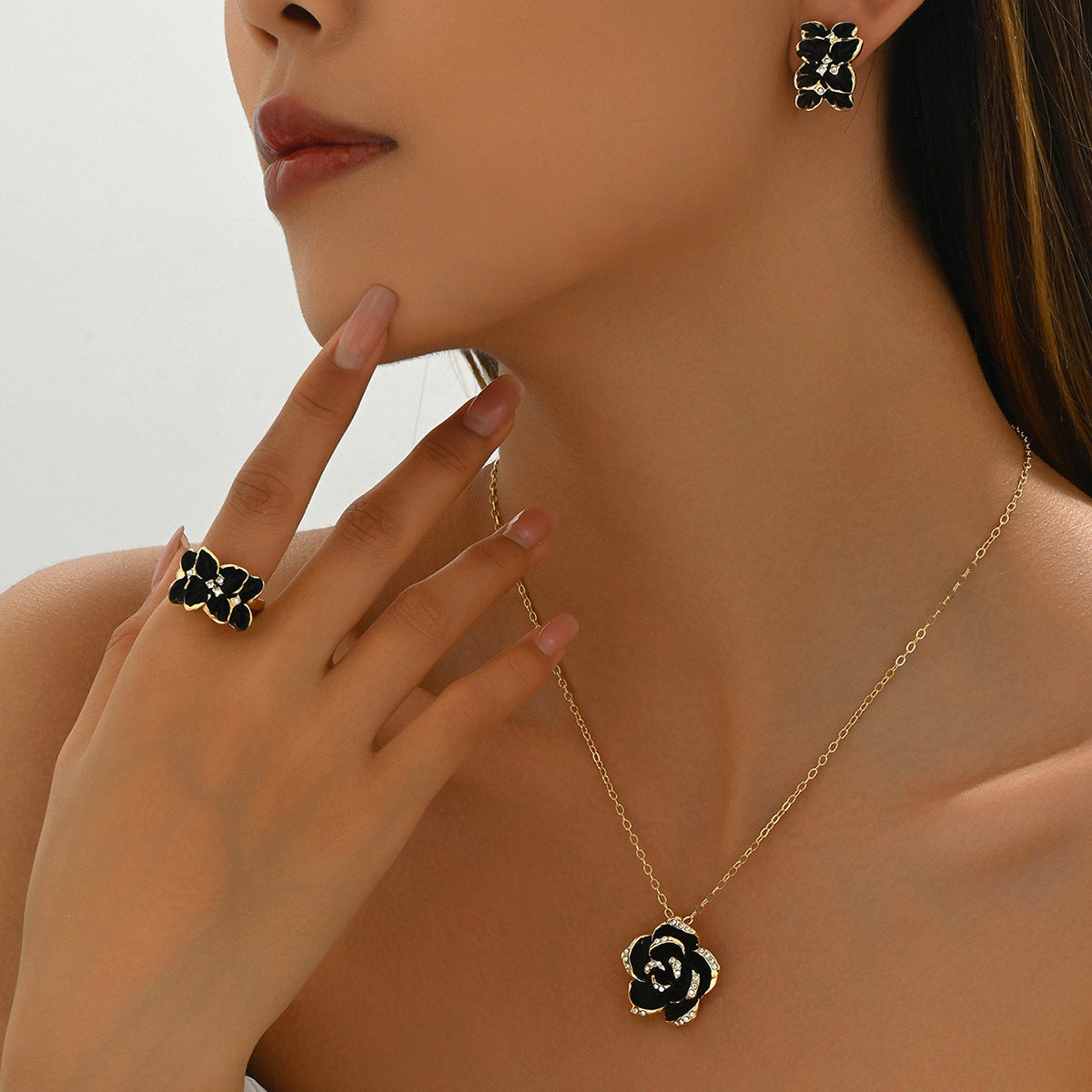 Model wearing a gold chain with black rose jewelry set pendant and matching ring and earrings