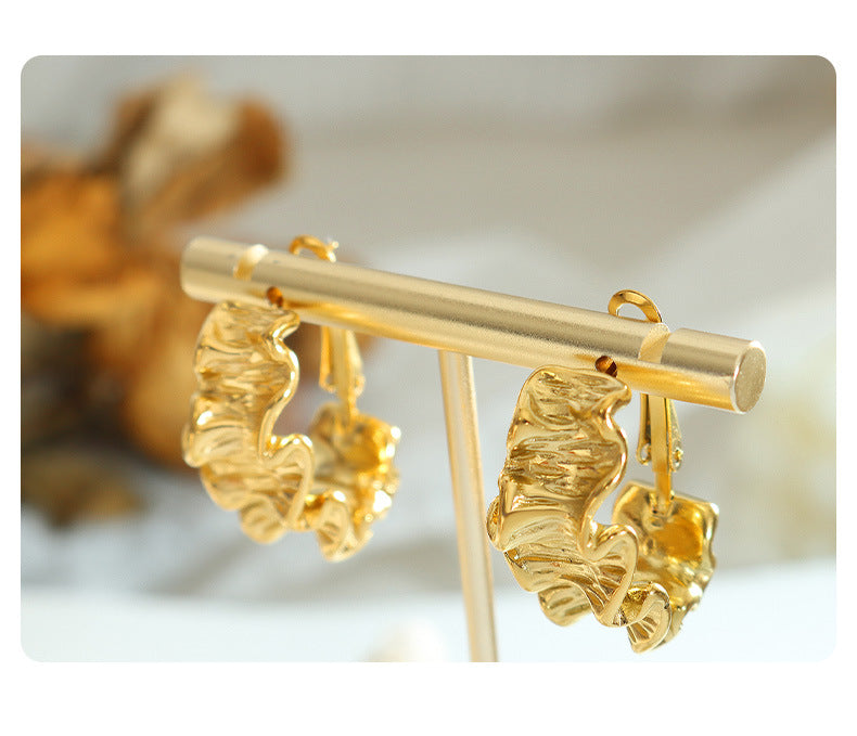 Fierce gold pleated earrings for women displayed on a gold stand with soft background