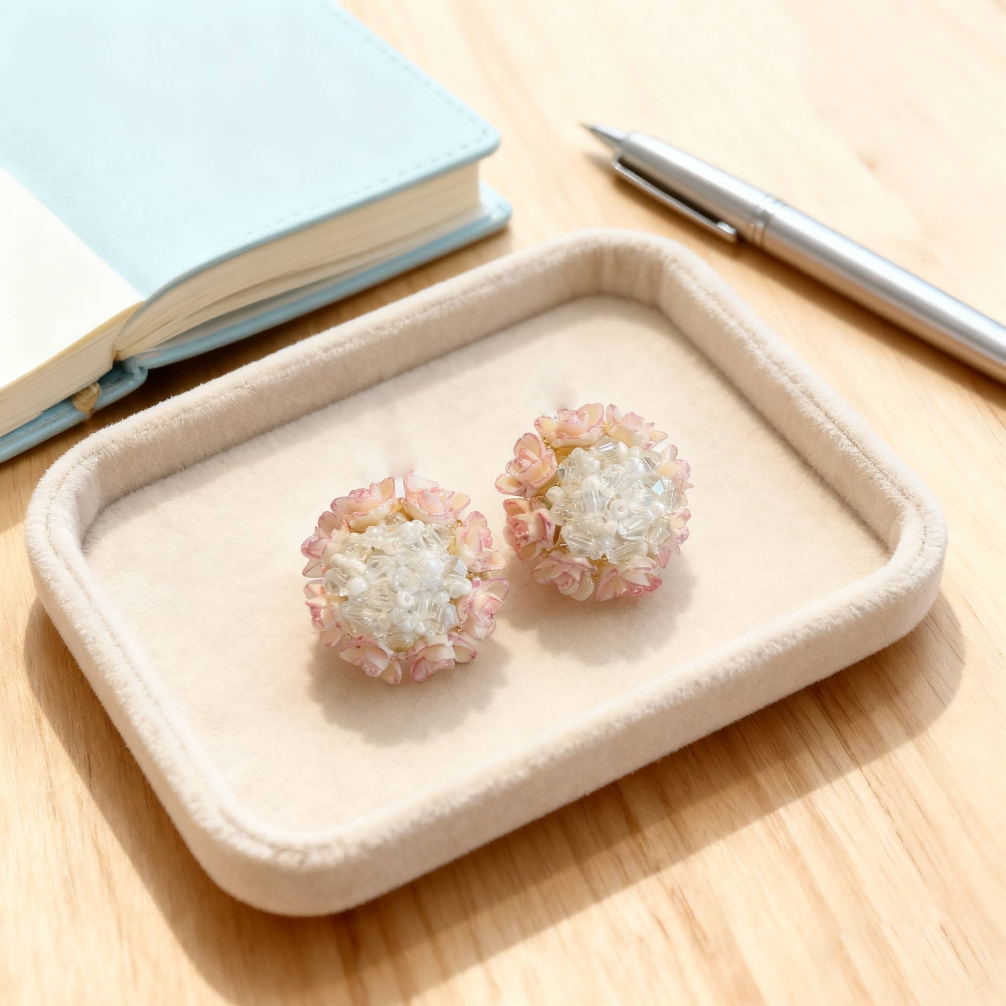5 Senses floral bead stud earrings displayed on a soft tray next to a notebook and pen