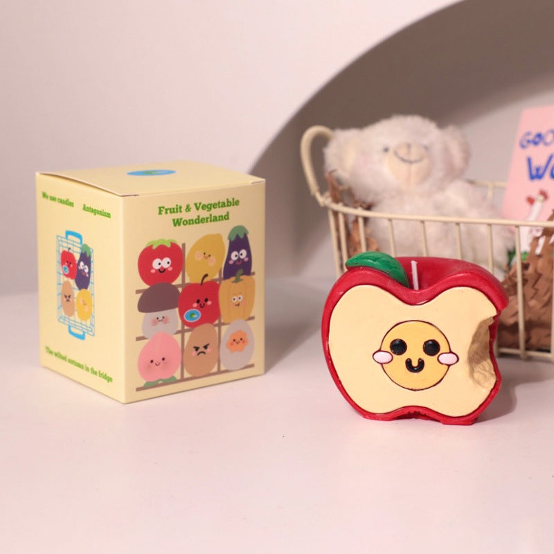 Hyper realistic food candle shaped like a smiling bitten apple with packaging box and teddy bear in background