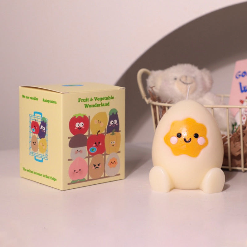 Cute hyper realistic food candle shaped like a smiling egg with a star yolk next to colorful fruit and vegetable box