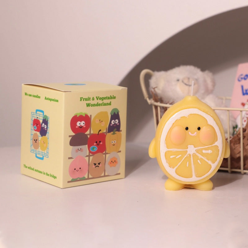 Cute yellow hyper realistic food candle shaped like a smiling lemon slice beside a colorful fruit and vegetable themed box