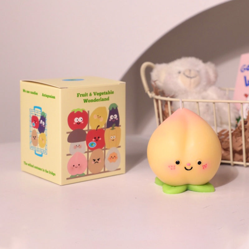 Cute hyper realistic food candle shaped like a smiling peach with rosy cheeks next to colorful cartoon fruit box