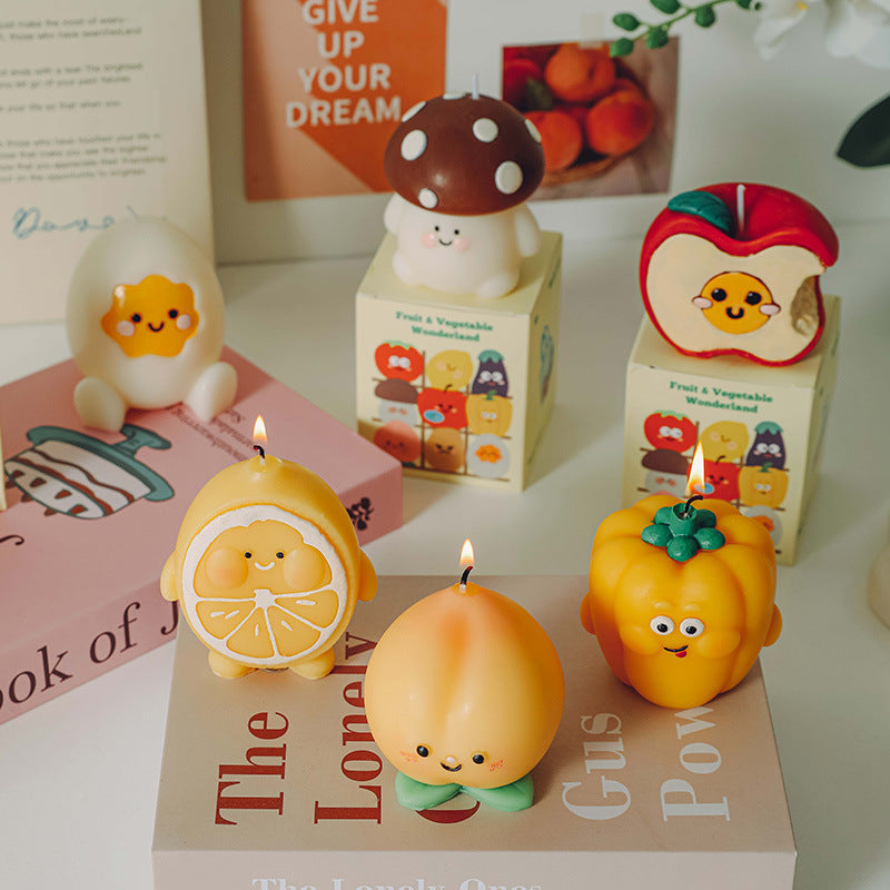 Set of hyper realistic food candle designs including lemon, peach, pumpkin, mushroom, apple, and egg candles with smiling faces