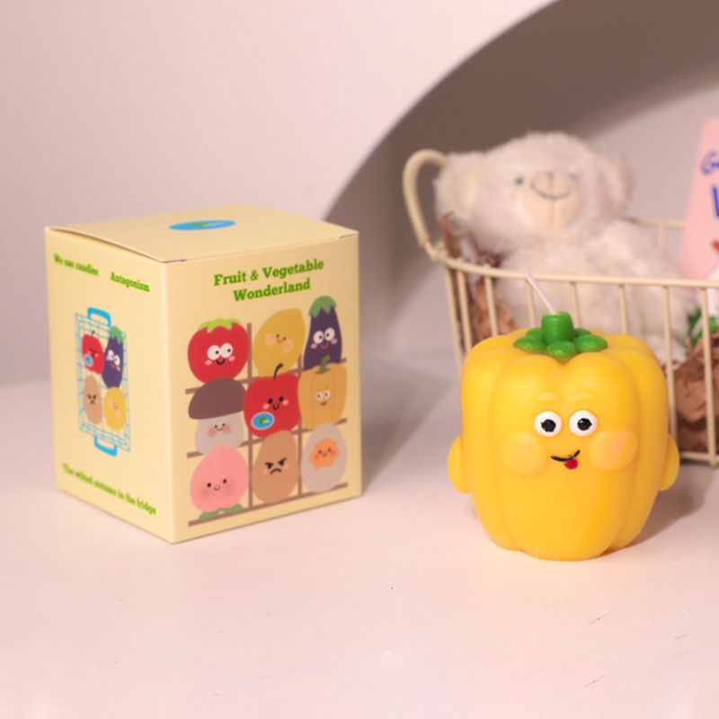 Yellow bell pepper hyper realistic food candle with cute face and packaging box on white surface