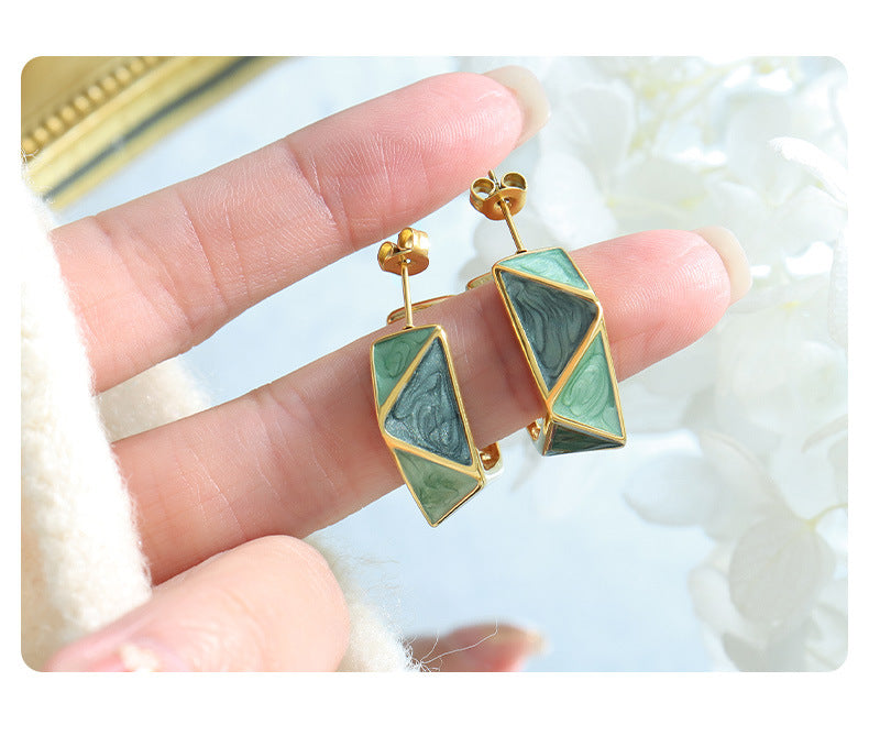 Calm geometric enamel earrings with green and gold tones held between fingers