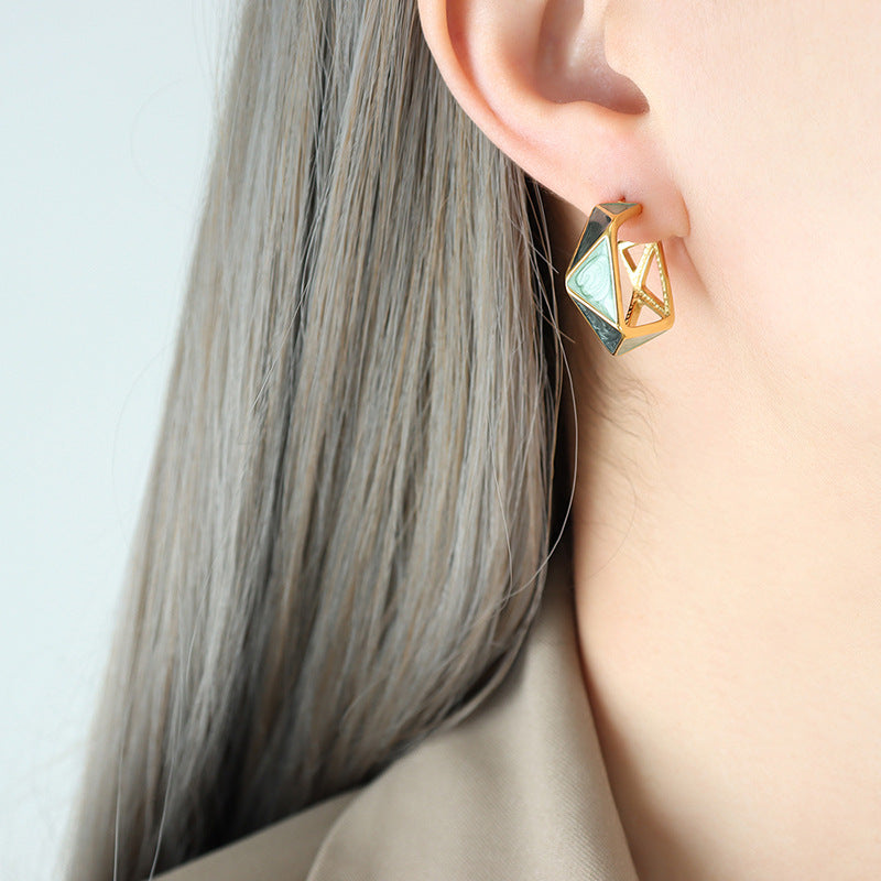 Gold and green geometric enamel earrings worn on ear with straight gray hair background