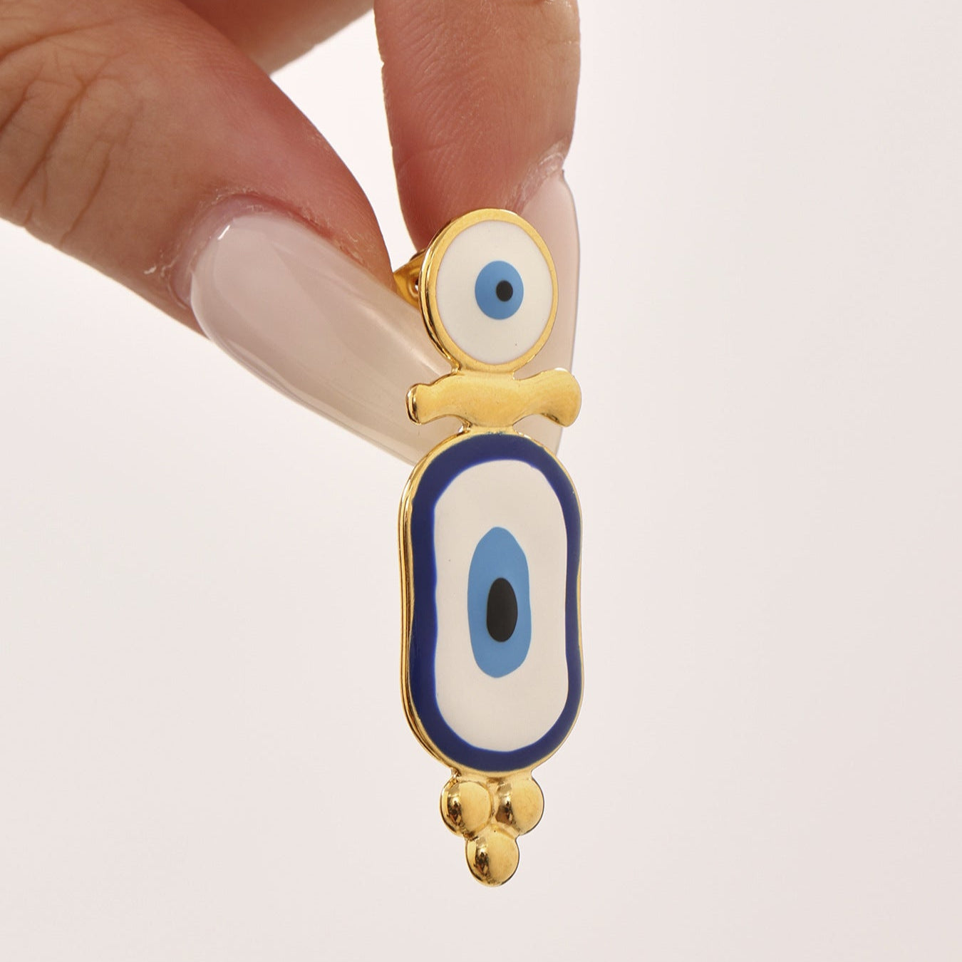 Hand holding a single gold Anxious blue evil eye earrings with detailed blue and white design