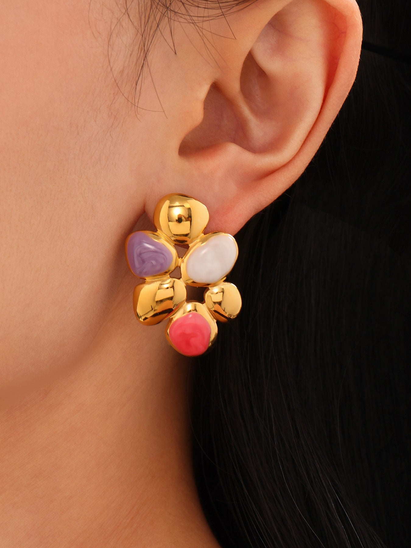 Close-up of ear wearing irregular enamel earrings with gold, purple, white, and pink accents