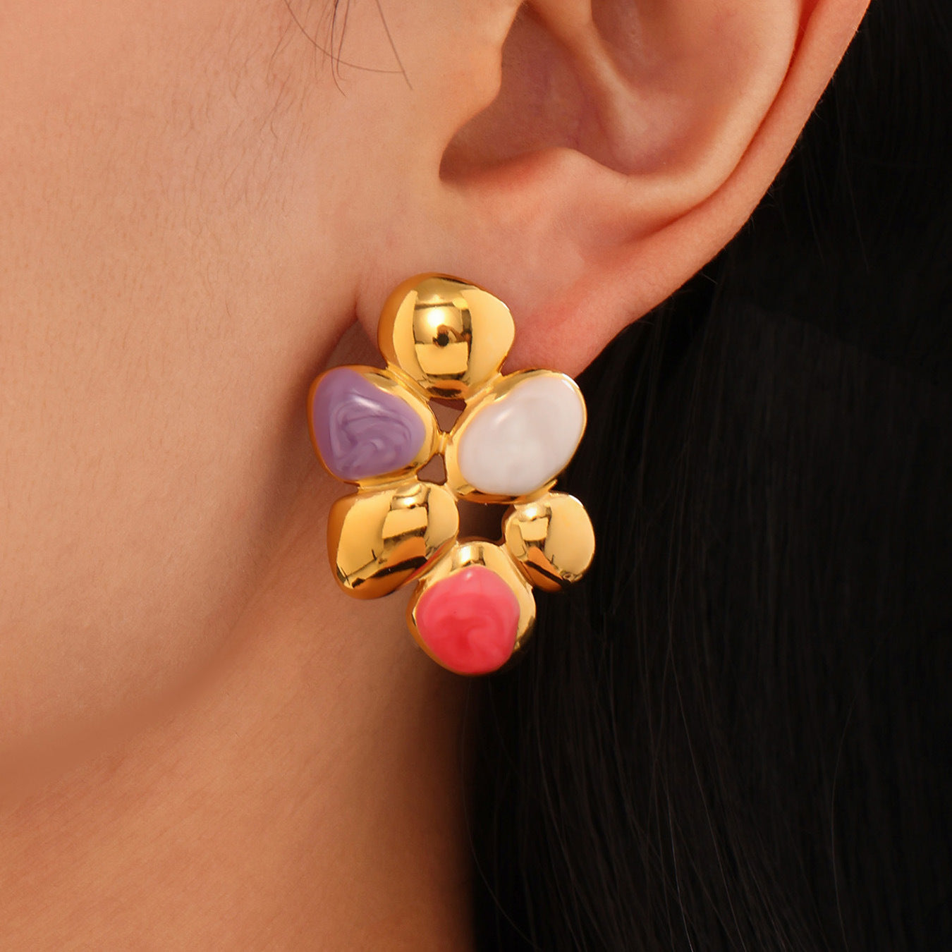 Close-up of irregular enamel earrings with gold and colorful enamel accents worn on ear