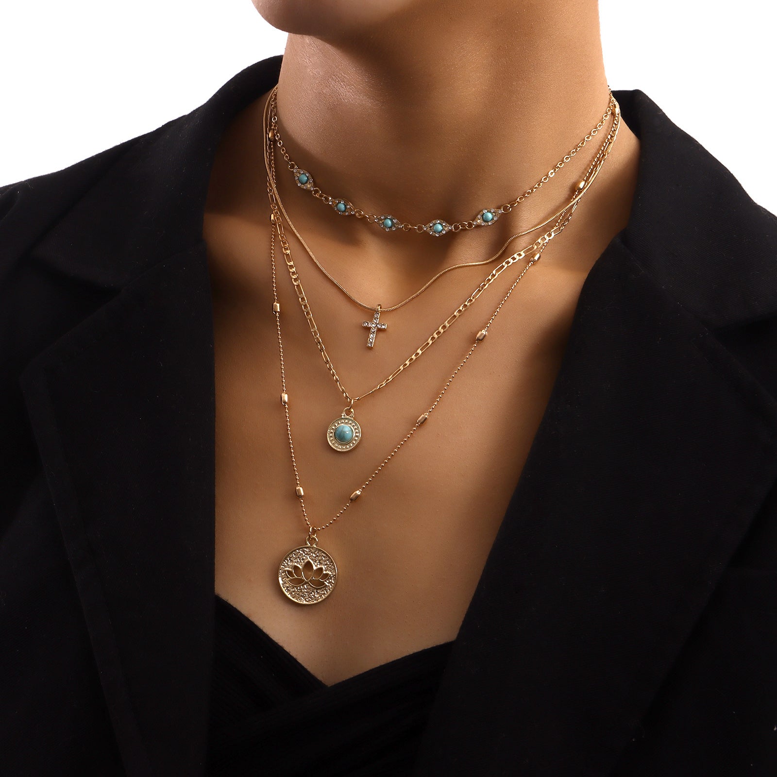 Gold multi-layered spiritual necklace with turquoise accents and cross pendant on model wearing black blazer