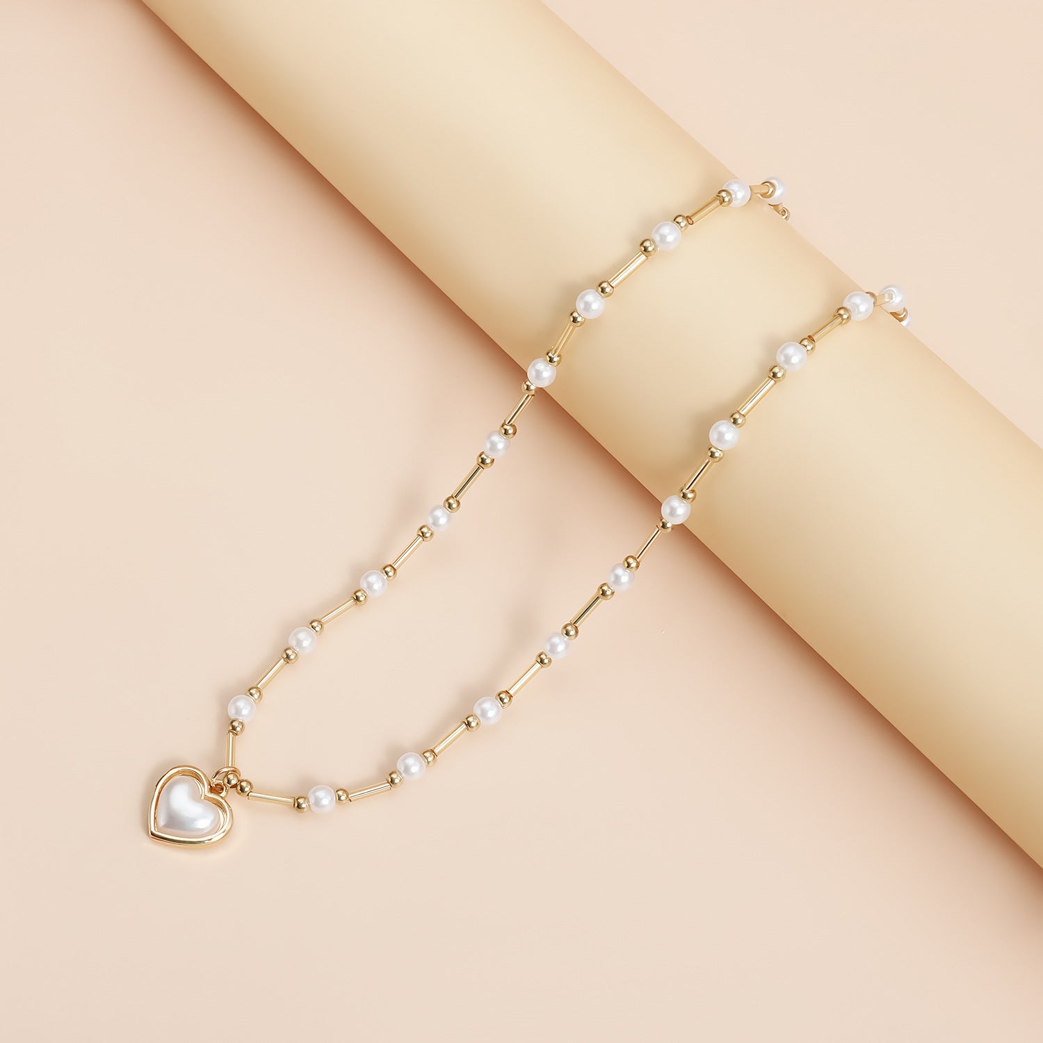 Elegant heart pearl necklace with gold links and a heart-shaped pearl pendant displayed on a beige background