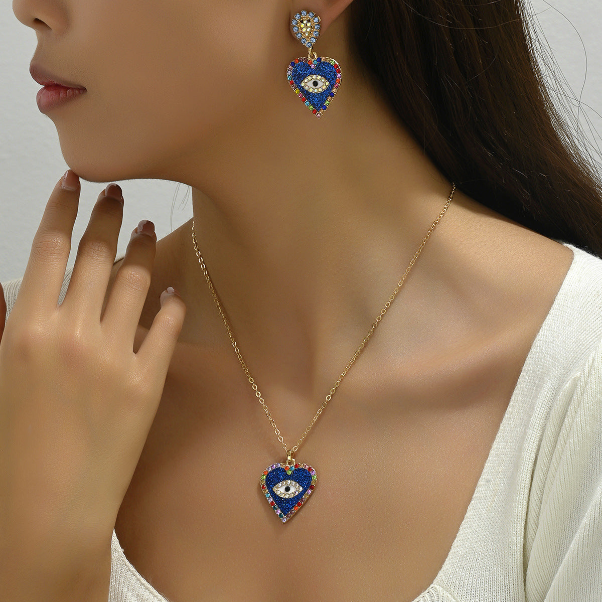 Model wearing blue evil eye jewelry set with heart shaped pendant necklace and matching drop earrings
