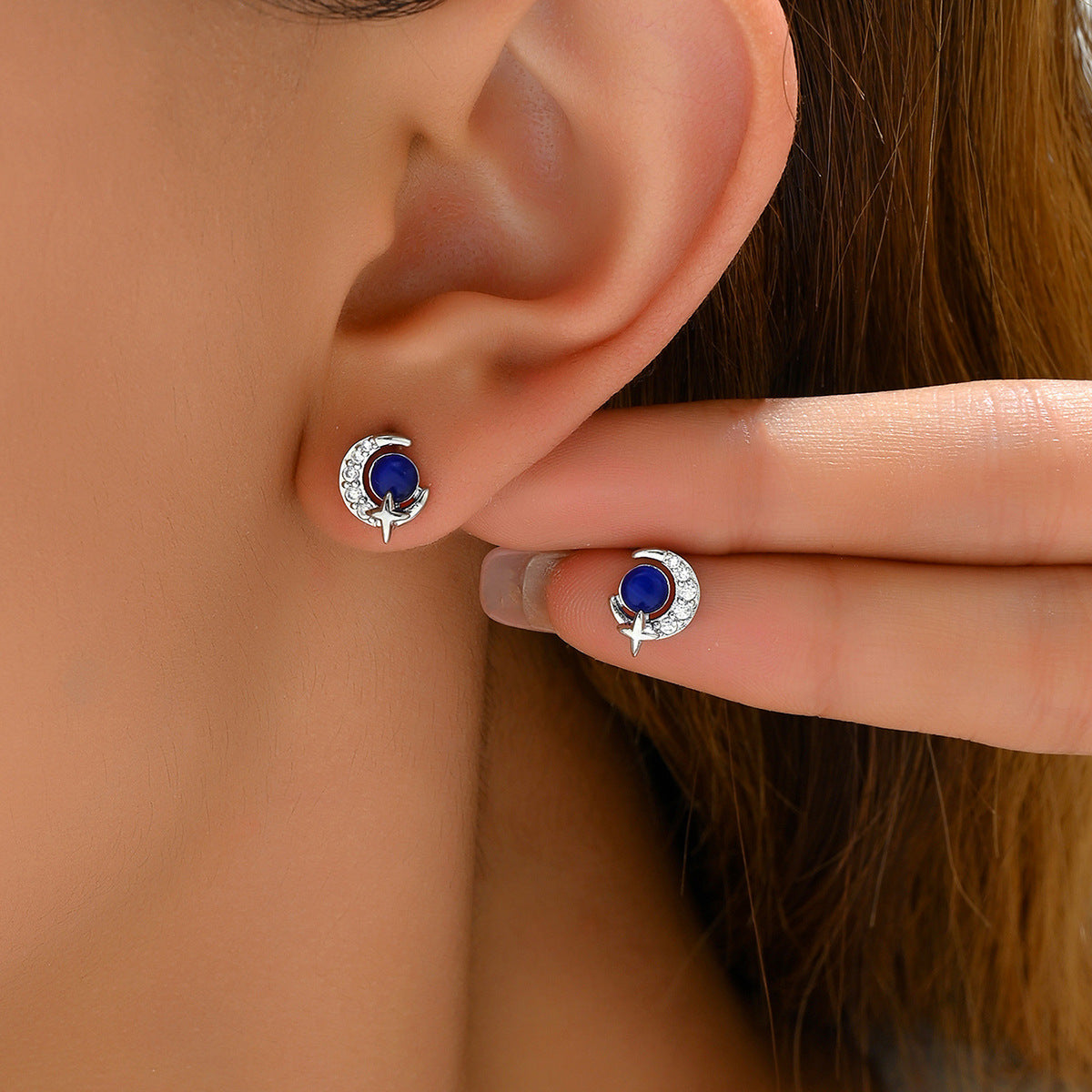 Silver crescent moon with blue center and clear crystals on ear, crescent moon star stud earrings shown