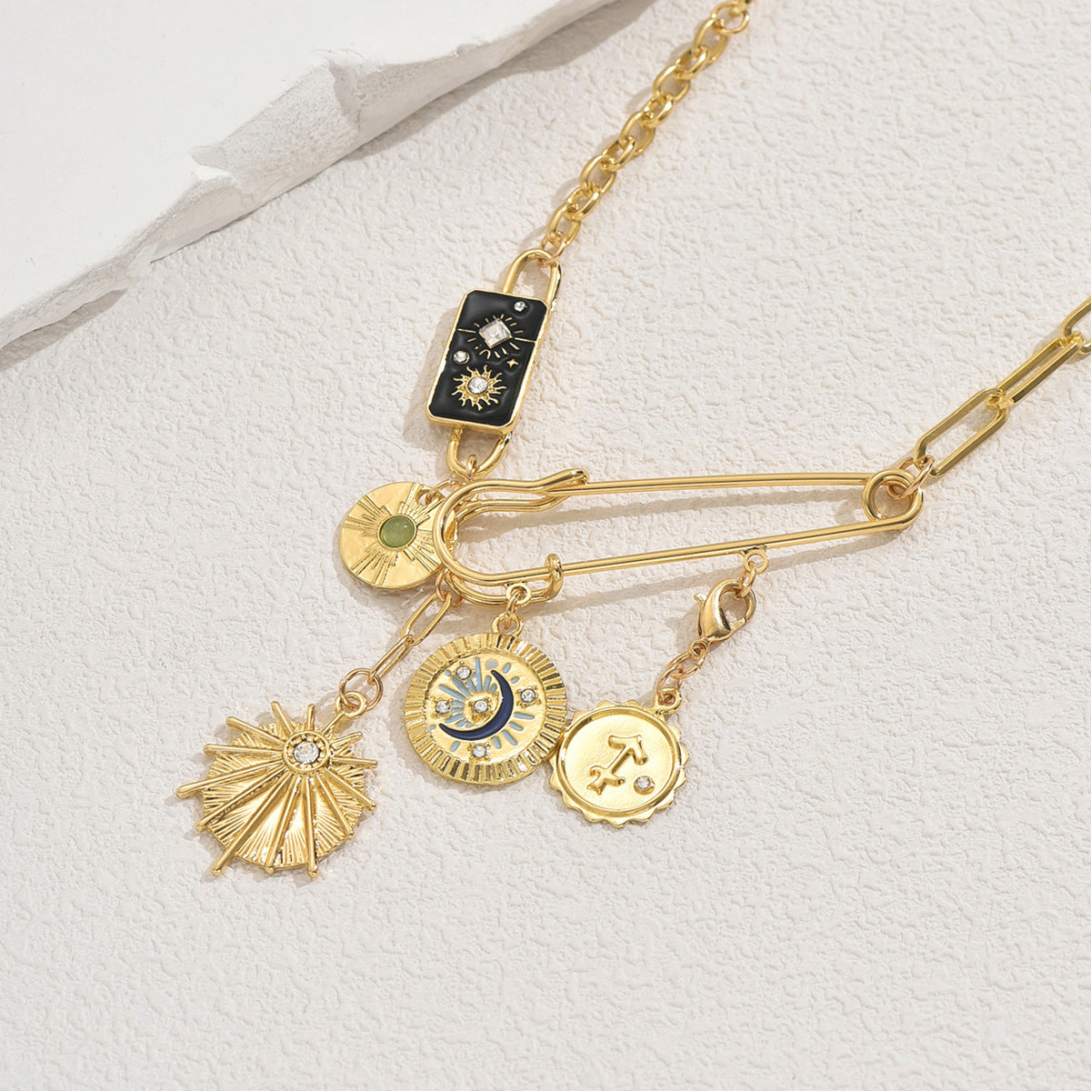 Layered gold chain with safety pin and celestial charms including enamel moon and sun gold sun moon pendant necklace