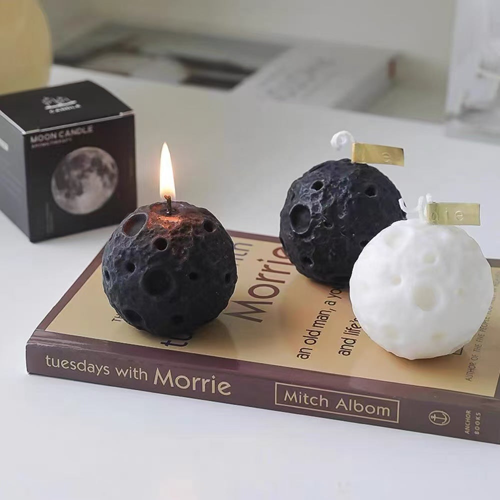 Lunar soy candle shaped like the moon in black and white colors displayed on a book with flame lit on one candle
