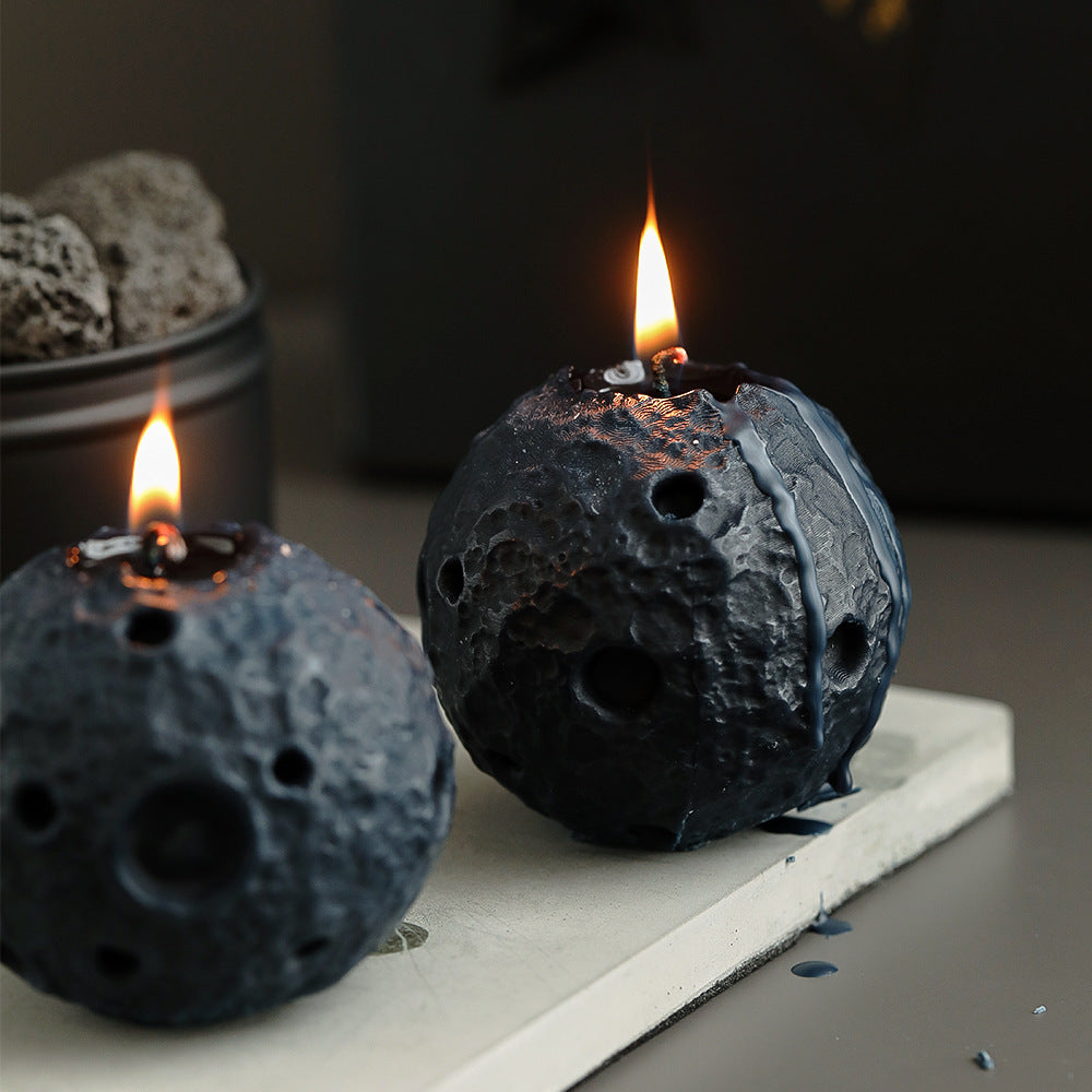 Lunar soy candle shaped like a cratered moon with a burning flame on a white surface