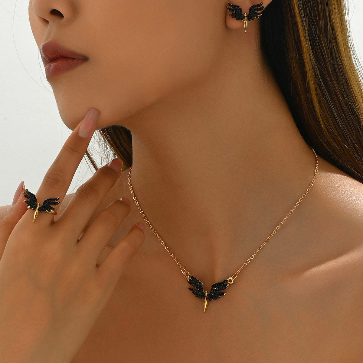 Model wearing black angel wings jewelry set necklace ring and earrings with gold chain and spike for edgy everyday style