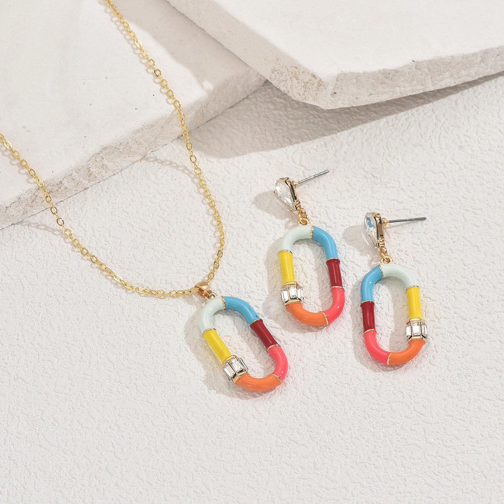 Gold chain colorful enamel necklace with matching multicolor enamel link earrings on textured white background