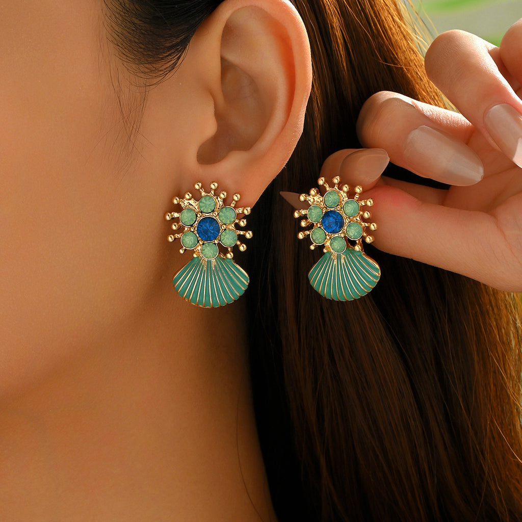 Close up of gold floral stud earrings with turquoise gems and geometric green shell drop earrings on ear