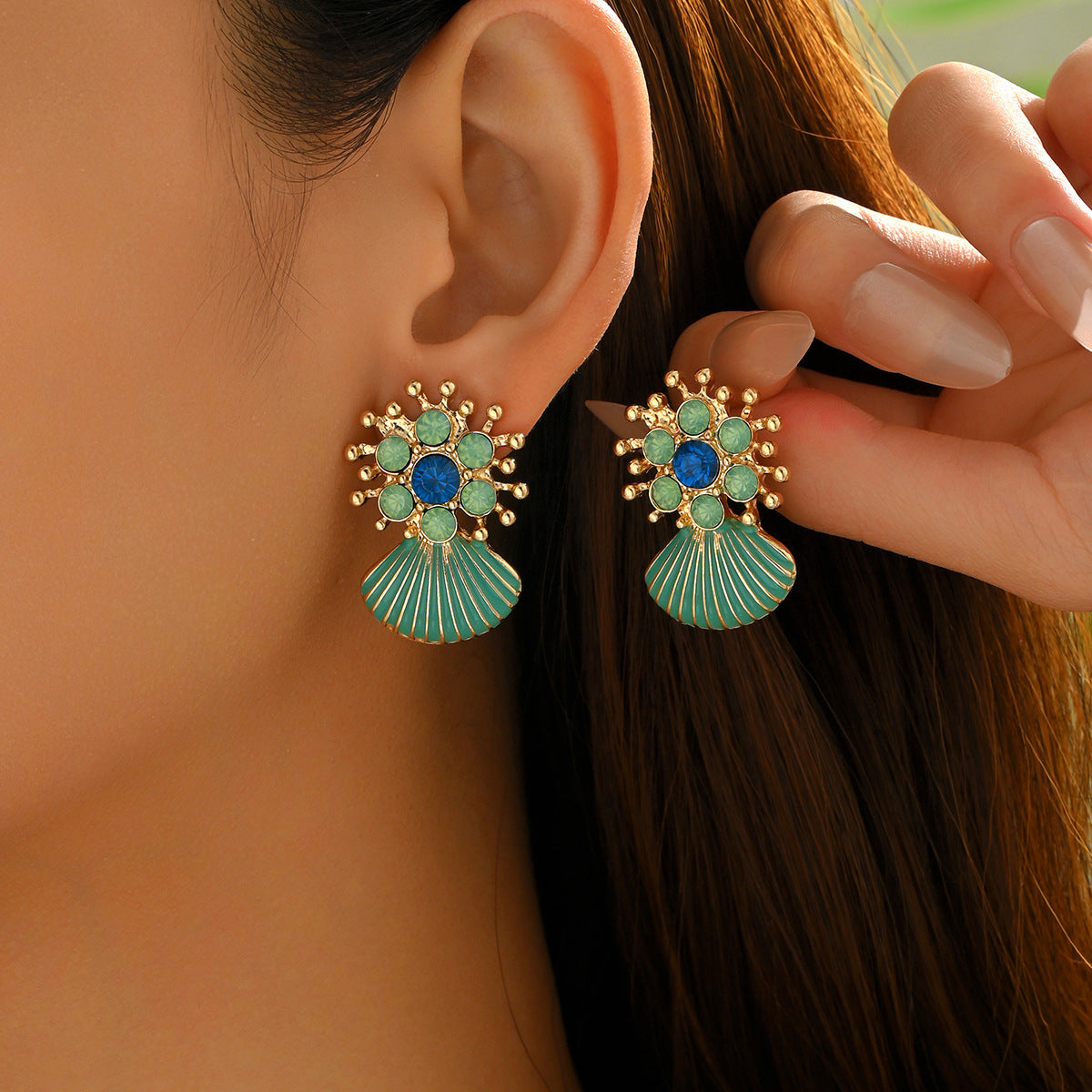 Close up of gold floral stud earrings with turquoise gems and geometric green shell drop earrings on ear