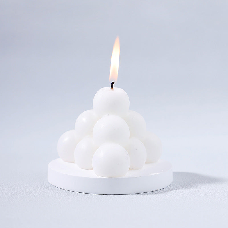 White modern decorative aromatherapy candle shaped like stacked spheres on a round base with a lit wick