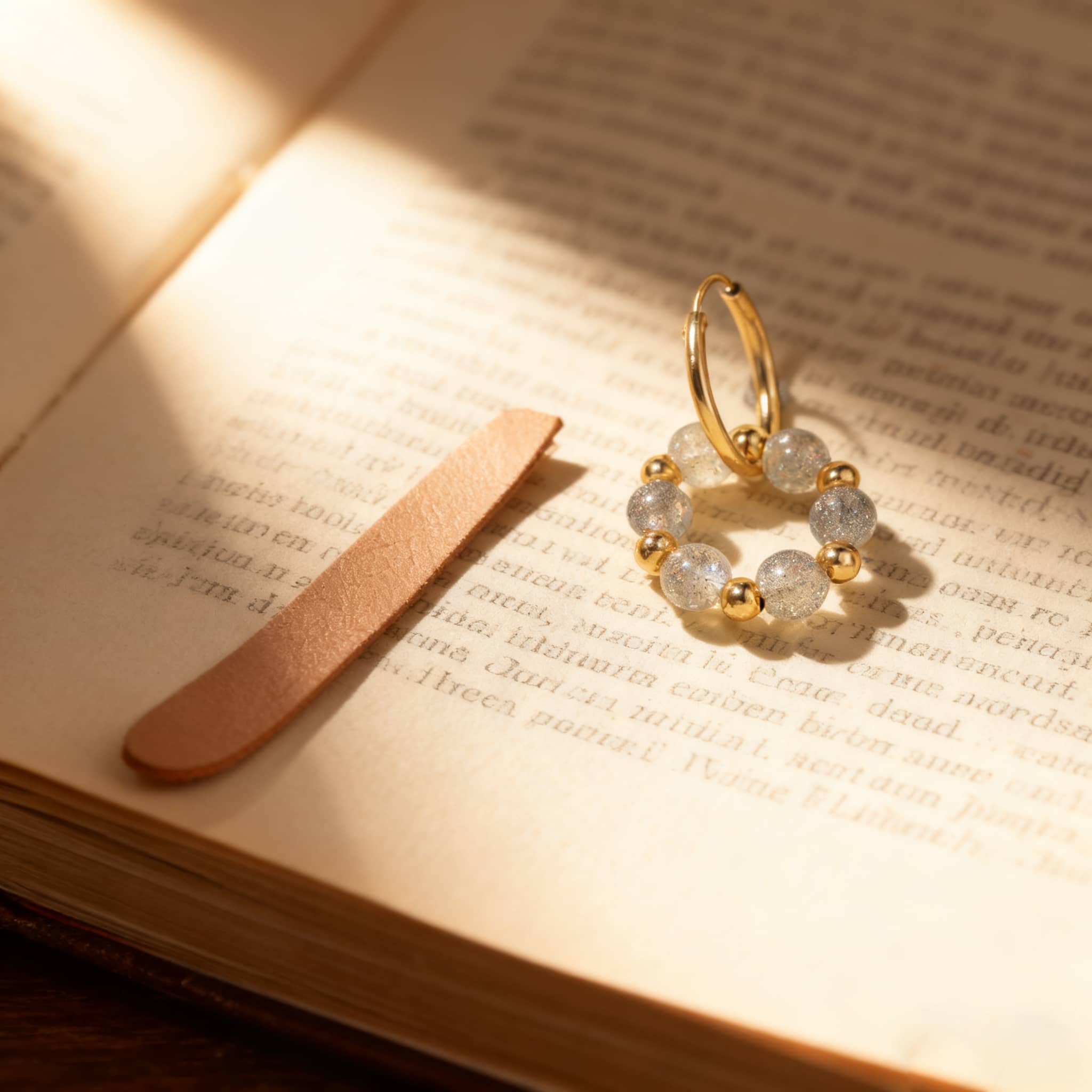 5 Senses moonstone anxiety earrings with gold accents and soft gray beads on a book