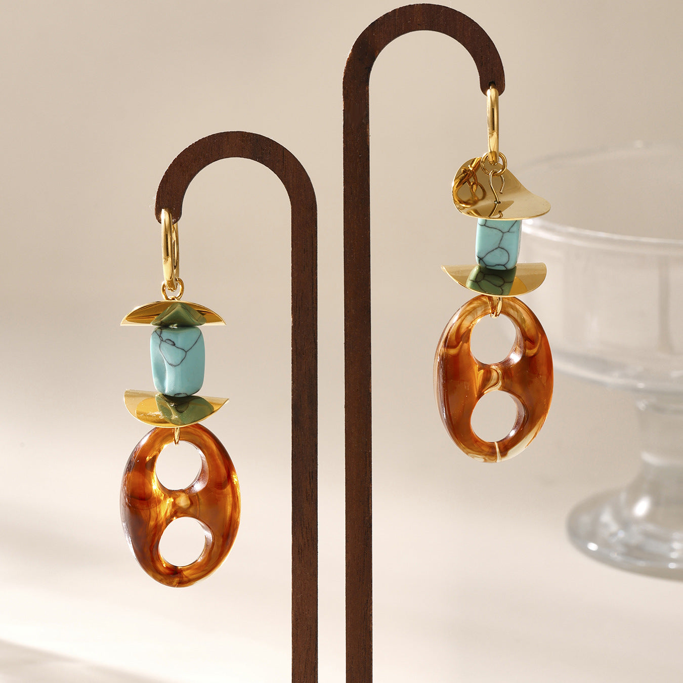 Calm oval resin stud earrings with turquoise and gold accents displayed on a wooden stand