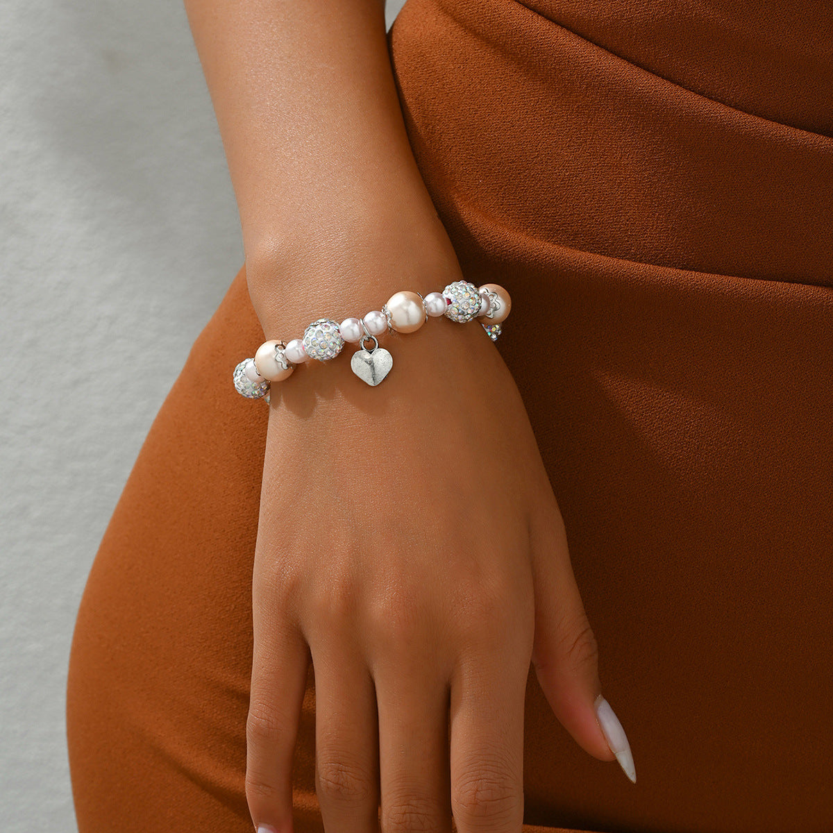 Elegant pearl bead bracelet for women with heart charm worn on wrist with brown outfit