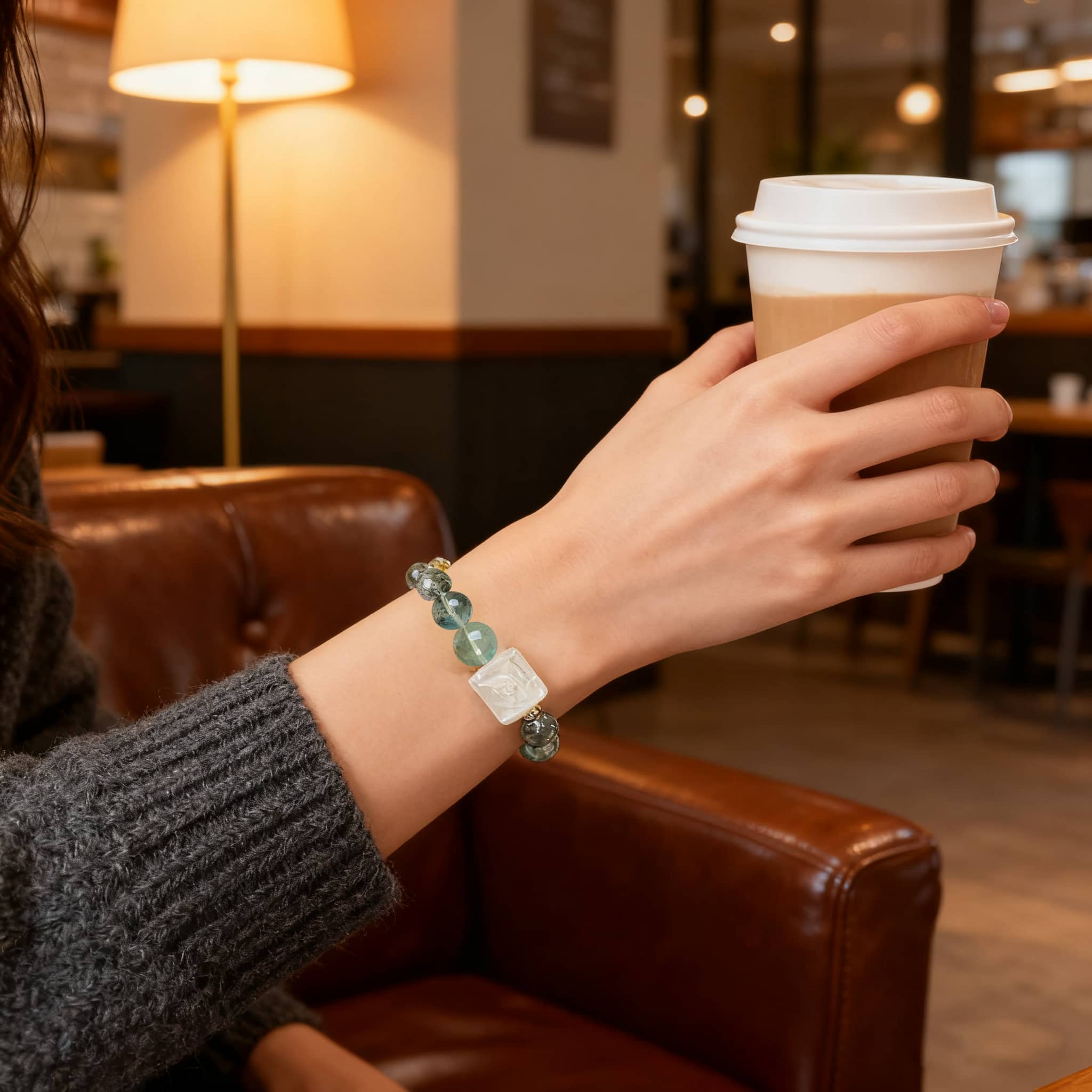 Elegant phoenix and peony gemstone bracelet worn on wrist while holding a coffee cup in a cozy cafe setting