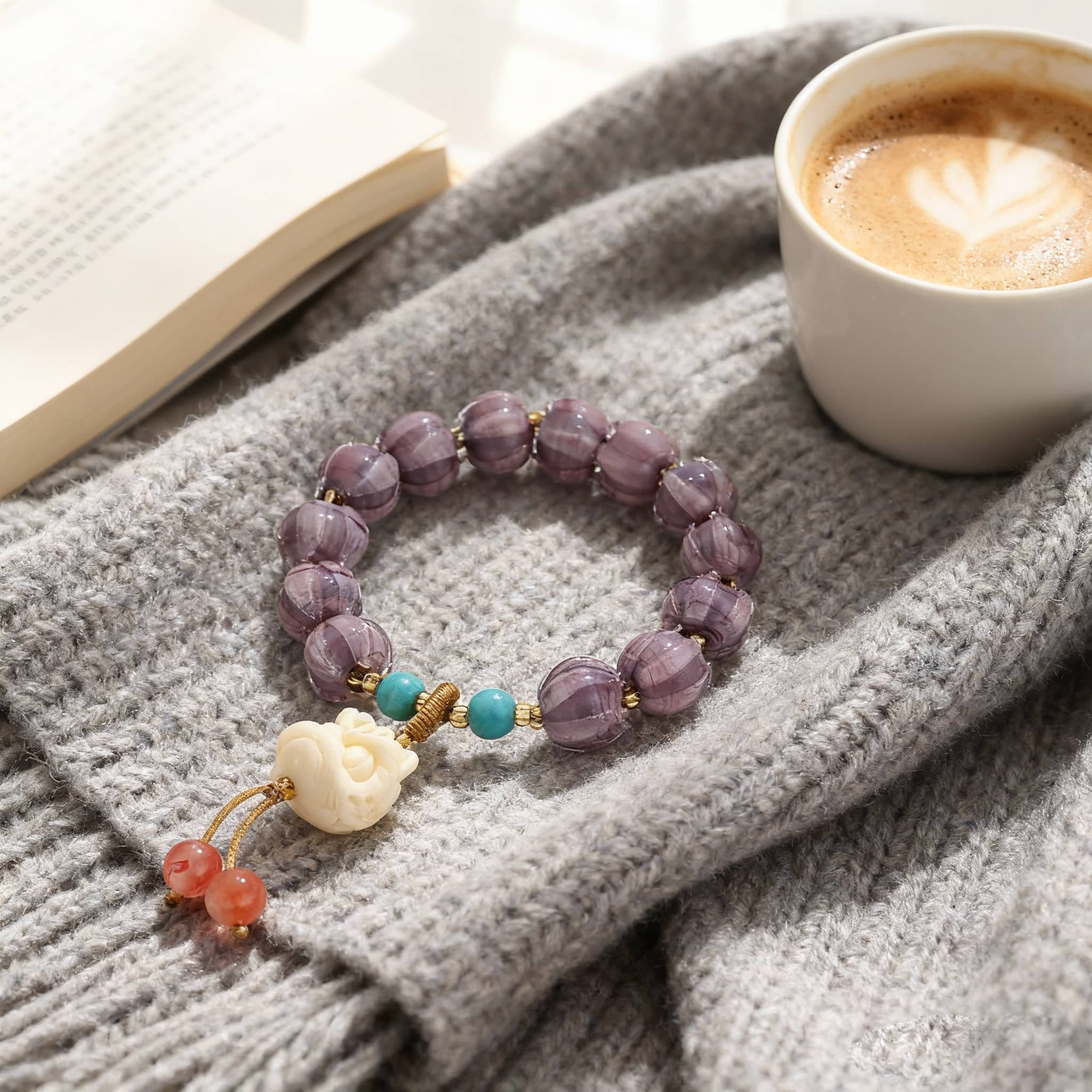 Purple gemstone self-care bracelet with beads and a decorative charm on a cozy blanket with a coffee cup