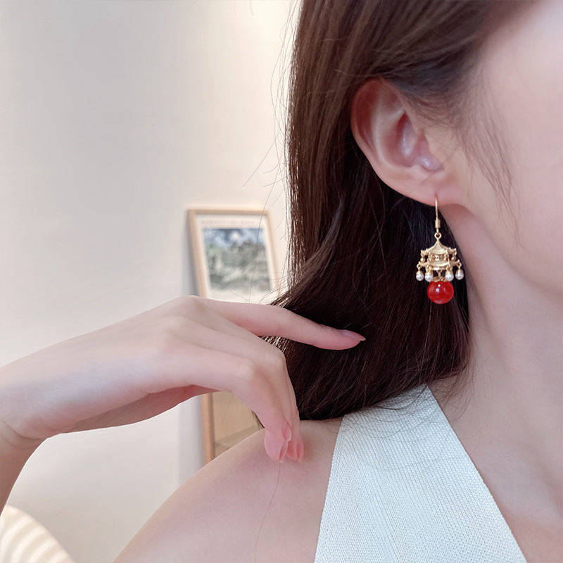 Calm red agate pearl earrings featuring gold detailing worn on ear with white sleeveless top