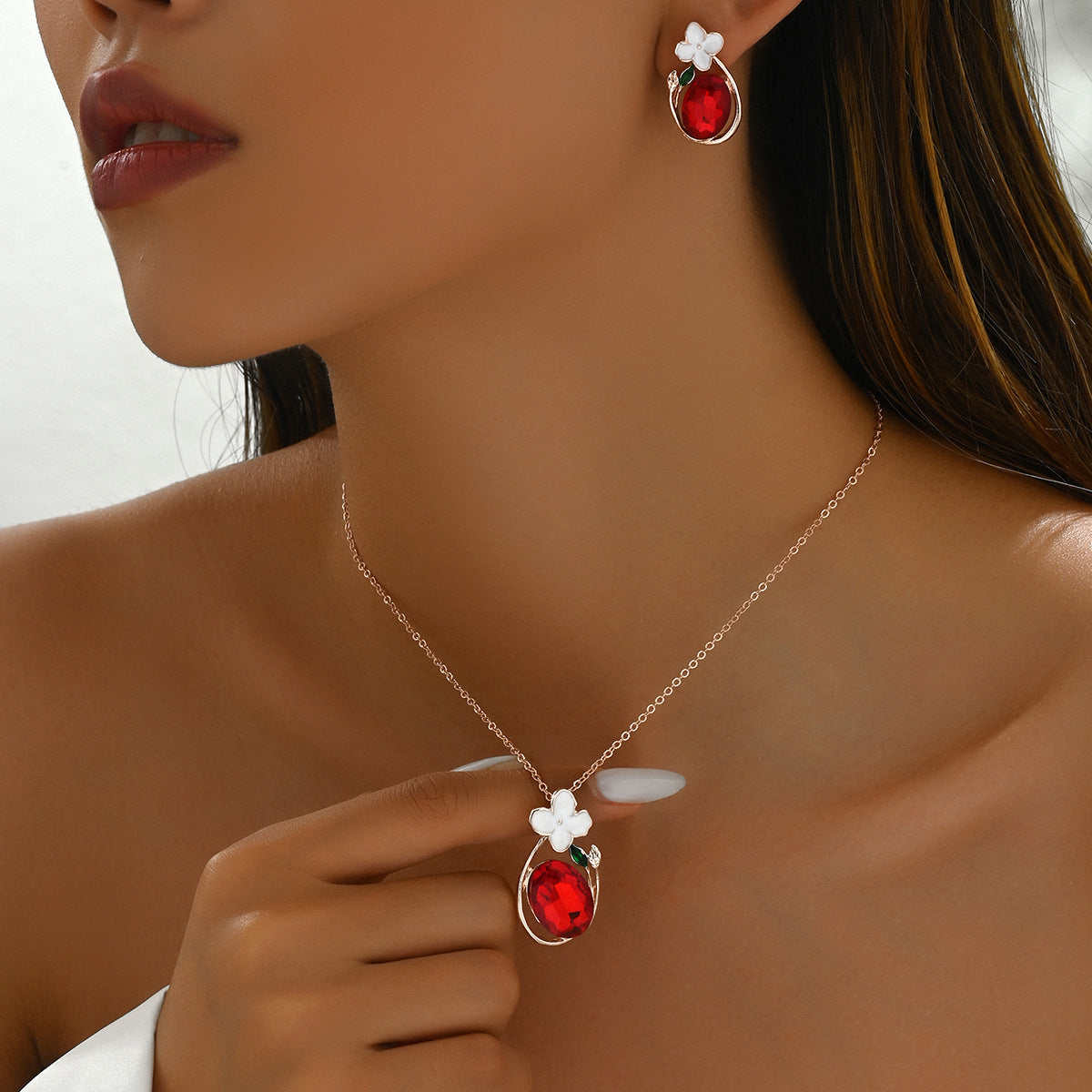 Model wearing red diamond necklace and earrings set teardrop red gem with white flower accent on rose gold chain