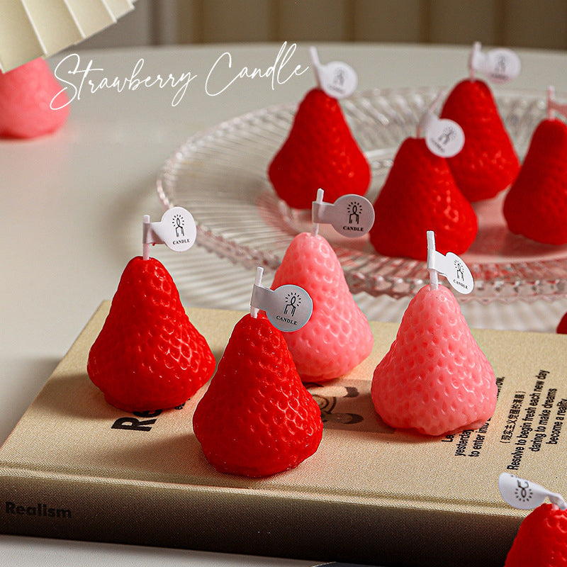 Self-love aromatherapy candle shaped like red and pink strawberries displayed on a book and plate